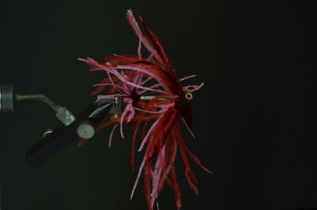 Side photograph of a source-labeled pink and red Intruder fly held against a black background